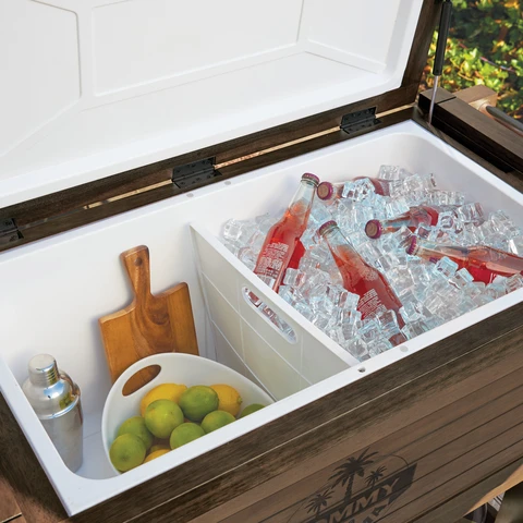 Open wood cooler with soda bottles on ice on one side and fresh limes in a bowl on the other side. 