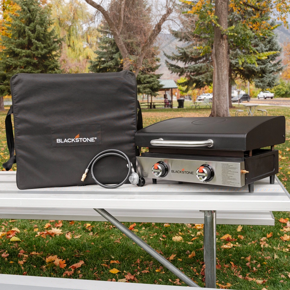 Carry bag, propane tank adapter hose, and 22 inch griddle shown on a picnic table at the park