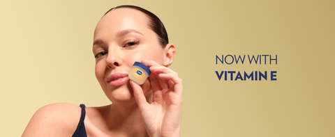 Woman holding a pot of Vaseline Crème Brûlée Lip Therapy Jelly next to text: Now with Vitamin E.