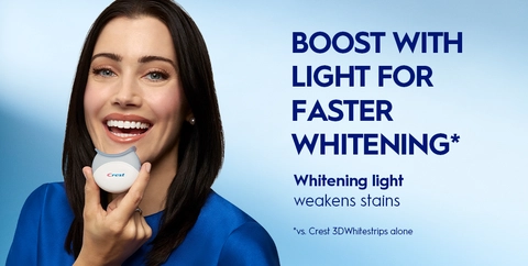 Woman smiling holding Crest LED Light up to her mouth. Boost with Light for Faster Whitening. Whitening Light Weakens Stains.