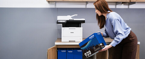 Woman removing Brother Genuine TN920 toner box from office cabinet, to replace in Brother business monochrome laser all-in-one printer