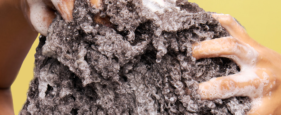 Hands massaging thick shampoo lather through dark textured hair root to ends.
