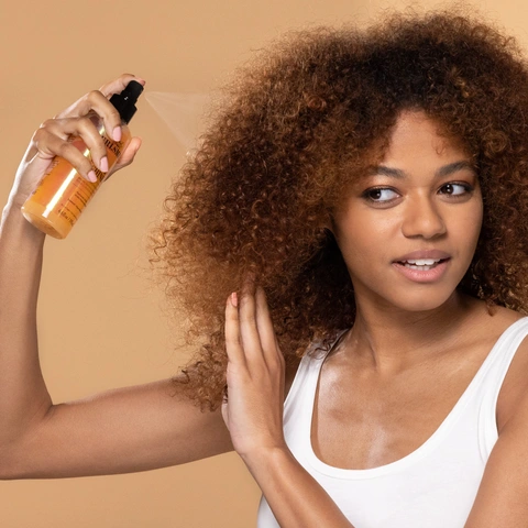 Model holding bottle to spray and mist sparingly throughout dry hair to reactivate your curls.