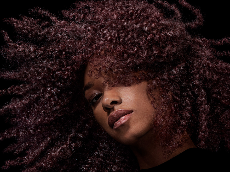 Model with coily brown hair styled with Dyson Chitosan styling products.