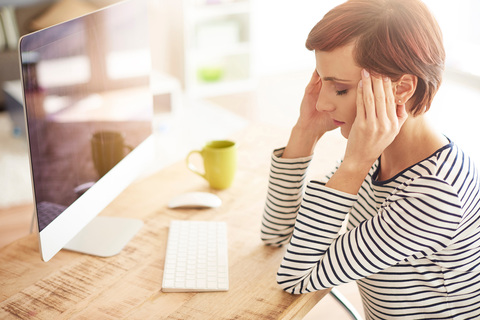 woman with headache  in front of computer holdin
