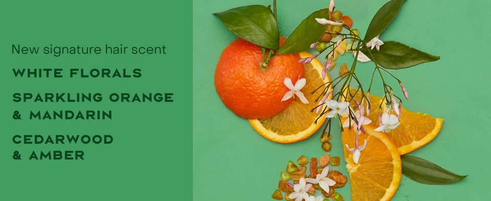 Text reads: "New signature hair scent. WHITE FLORALS, SPARKLING ORANGE &amp; MANDARIN, CEDARWOOD &amp; AMBER." Background features oranges and florals.