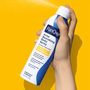 A hand holding and spraying PanOxyl Acne Banishing Body Spray