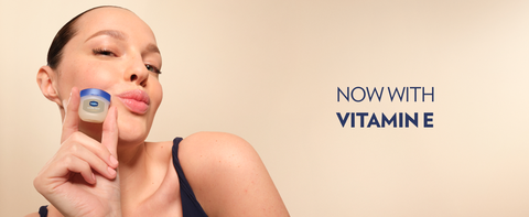 Woman holding a pot of Vaseline Lip Therapy Jelly next to text: Now with Vitamin E.