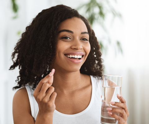 Photo: woman taking a fruit capsule with a glass of water.