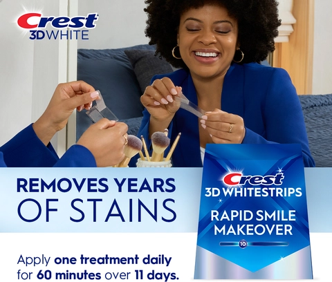 Reflection of woman in mirror smiling and peeling a Crest 3DWhitestrip. Removes Years of Stains..