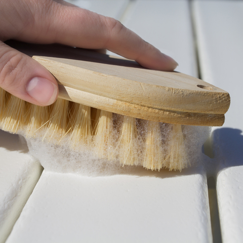 Hand holding soapy brush cleaning lumber