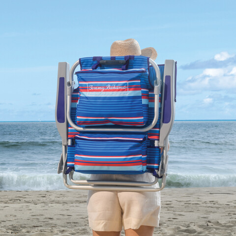 Woman carrying beach chair as a backpack walking down a beach.