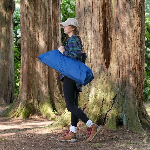 Young woman walking through the woods carrying chair storage bag over her shoulder..