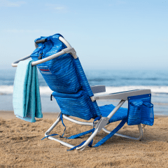 Profile of a beach chair with towel hanging of towel bar on the back of the chair on the beach. 