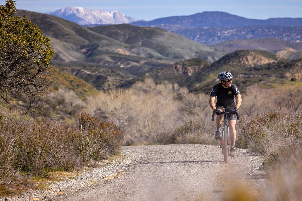 951 Gravel Bike riding along dirt trail with scenic snow covered mountains in background.