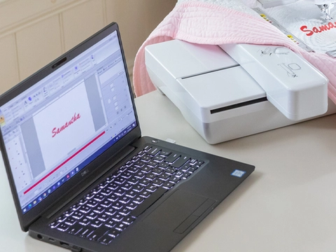 Machine with pink fabric and laptop on desk 