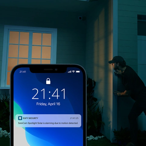 Example of eufy app notification shown on smartphone in foreground of image as background image conveys stranger approaching a home front door at night.
