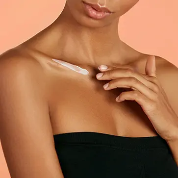 Upper body shot of woman with beautiful brown skin applying a dollop of lotion onto her chest.