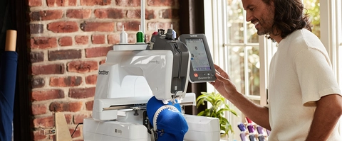 Man holding the machine screen, watching his blue cap project.