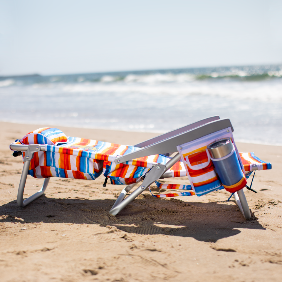 Stripped beach chair fully reclined on the beach with the ocean in the background. 