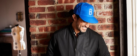 man standing against red brick wall, wearing a blue cap with letter &quot;B&quot; initial