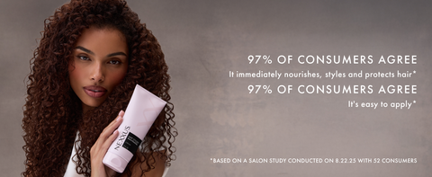Woman with curly dark hair holding a MVP Styler Cream tube next to her face on a beige background.