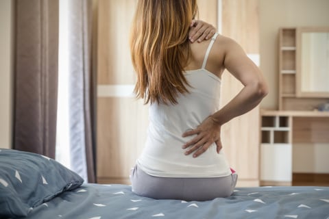 Woman sitting on bed, holding shoulder and back in pain