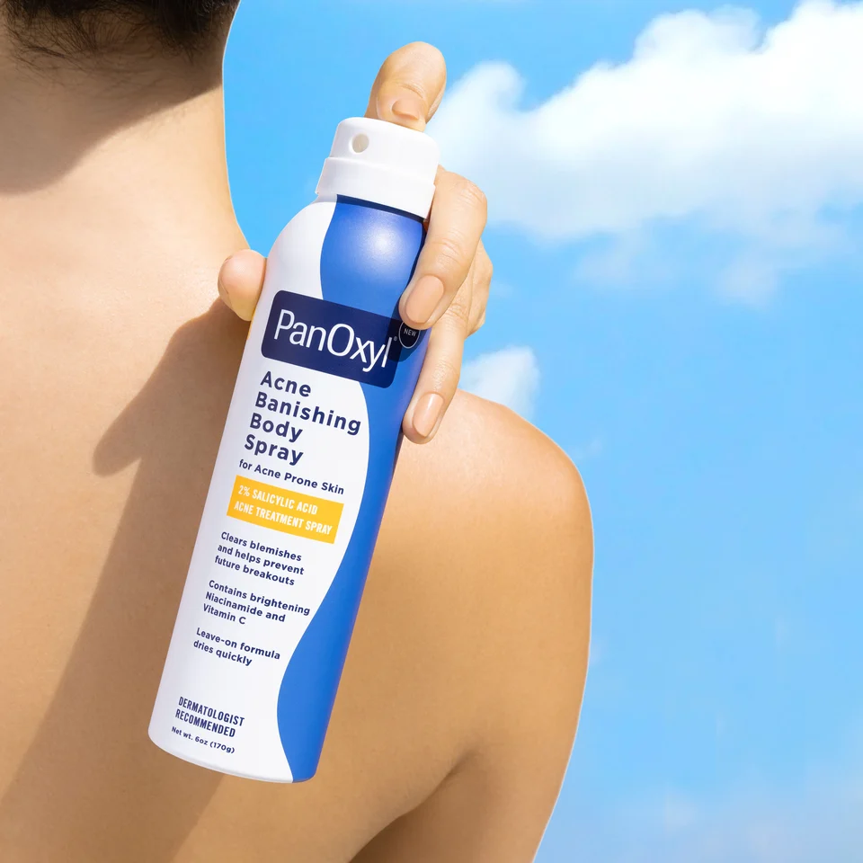 PanOxyl Acne Banishing Body Spray can being held against a back to show that it is used on the back and hard to reach places of the body.