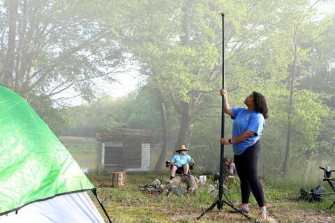 Outdoor camping scene of a female setting up the FLi OVER-LANDER Telescoping Area light