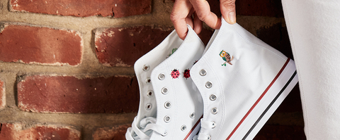 Woman holding a pair of white sneakers with embroidery patterns: lady bug and owl