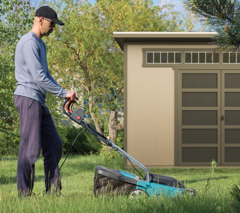 Man mowing grass with montague shed in background in backyard.