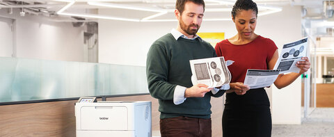 Two colleagues reviewing monochrome sales report document, printed from Brother business laser printer with Brother Genuine toner