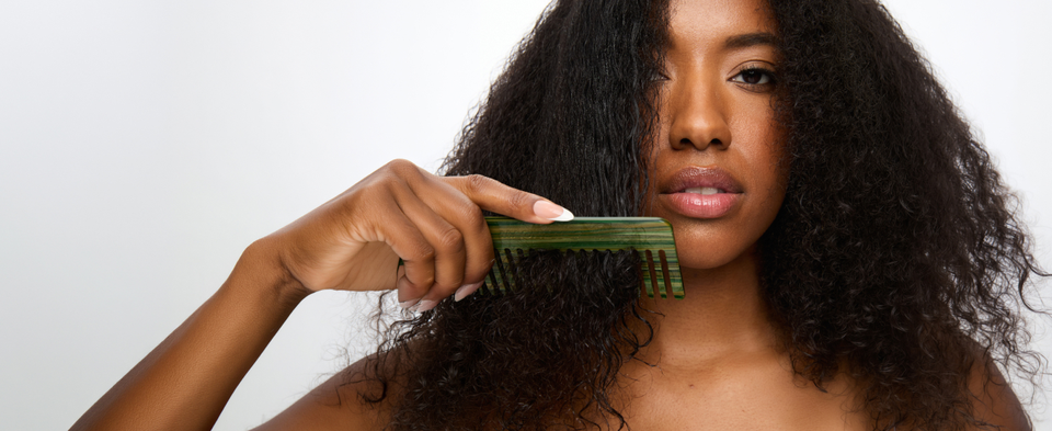 Comb applying SheaMoisture Prep Cream through damp hair on a green background.