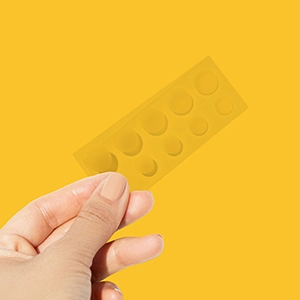 A hand holding a clear strip of ten translucent circular patches in two sizes
