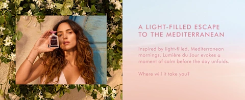 Person holding Moroccanoil Lumière du Jour perfume bottle outdoors with blooming flowers and Mediterranean-inspired setting