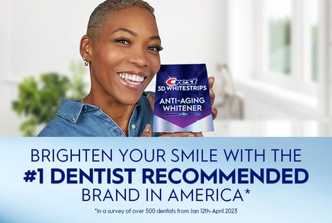 Woman smiling holding Crest 3DWhitestrips Anti-Aging Whitener pack. Brighten Your Smile with the #1 Dentist Recommended Brand in America.