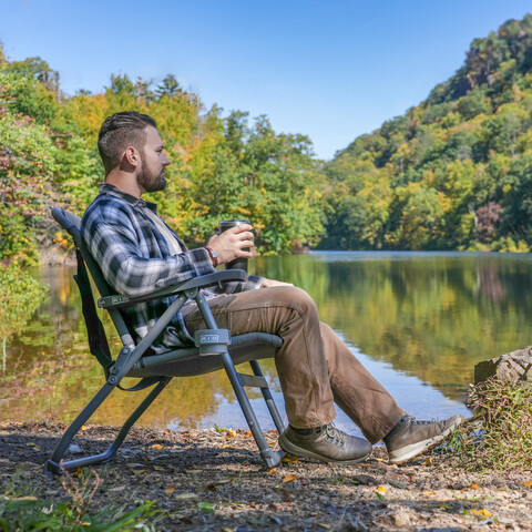 Young man sitting comfortably in chair by a lake.