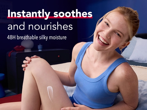 Woman smiling while applying Aquaphor cream to leg on bed, with text stating Instantly soothes and nourishes with 48H breathable silky moisture