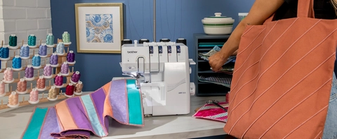 Air1800 on a table in sewing room, featuring finished projects. A woman carrying an rust color bag and AIR1800 with placemat project.