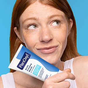A young woman holding a tube of PanOxyl Acne Creamy Wash near her face.