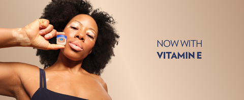 Woman holding a pot of Vaseline Cocoa Butter Lip Therapy Jelly next to text: Now with Vitamin E.