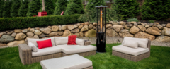 Paragon Outdoor Illume Propane Patio Heater in backyard setting next to outdoor furniture on lush green grass and stone backwall.