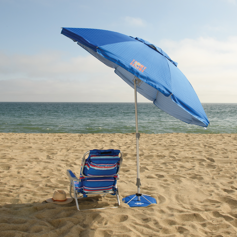 Beach chair under tilted umbrella on sandy beach.