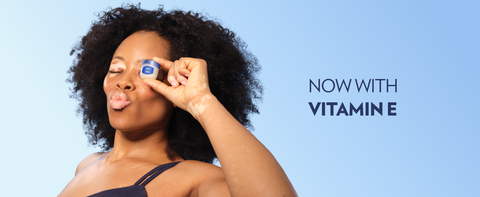 Woman holding a pot of Vaseline Original Lip Therapy Jelly next to text: Now with Vitamin E.