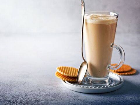 Latte in a tall cup in a saucer, with a spoon and two cookies around it.