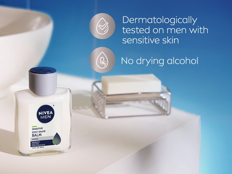 NIVEA MEN Sensitive Post Shave Balm on white shelf with shaving brush, blue background. Icons highlight: Dermatologically tested on men with sensitive skin and No drying alcohol formula