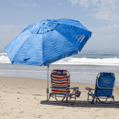 Blue, open, tilted beach umbrella on the sand with two beach chairs. 