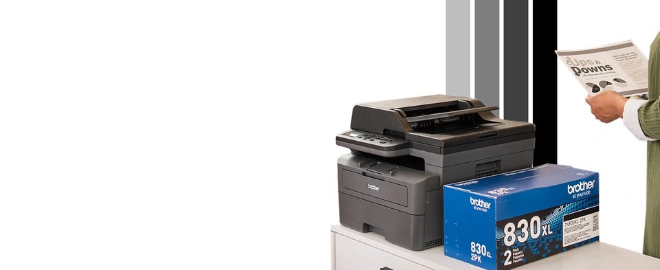 Persona en una pequeña oficina revisando un documento en blanco y negro impreso con la impresora láser 3 en 1 Brother DCP-L2640DW con alimentación automática de documentos, sentada sobre archivadores, junto a un paquete doble de tóner negro de alto rendimiento TN830XL2PK de repuesto original de Brother
