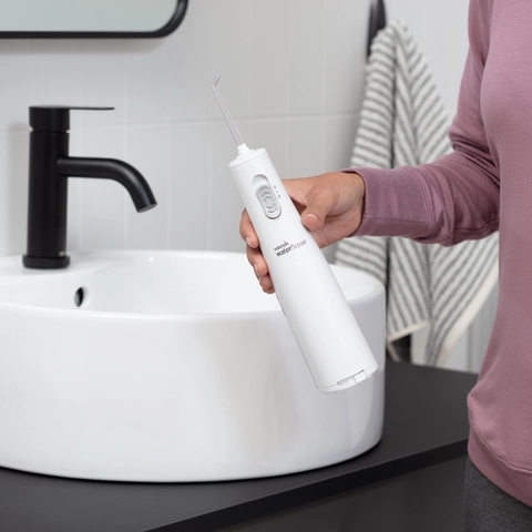 Hand Holding White Cordless Express Water Flosser WF-02 in Bathroom