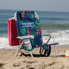 Tropical patterned Tommy Bahama branded beach chair with cup in cup holder and a towel on the back on the beach. 